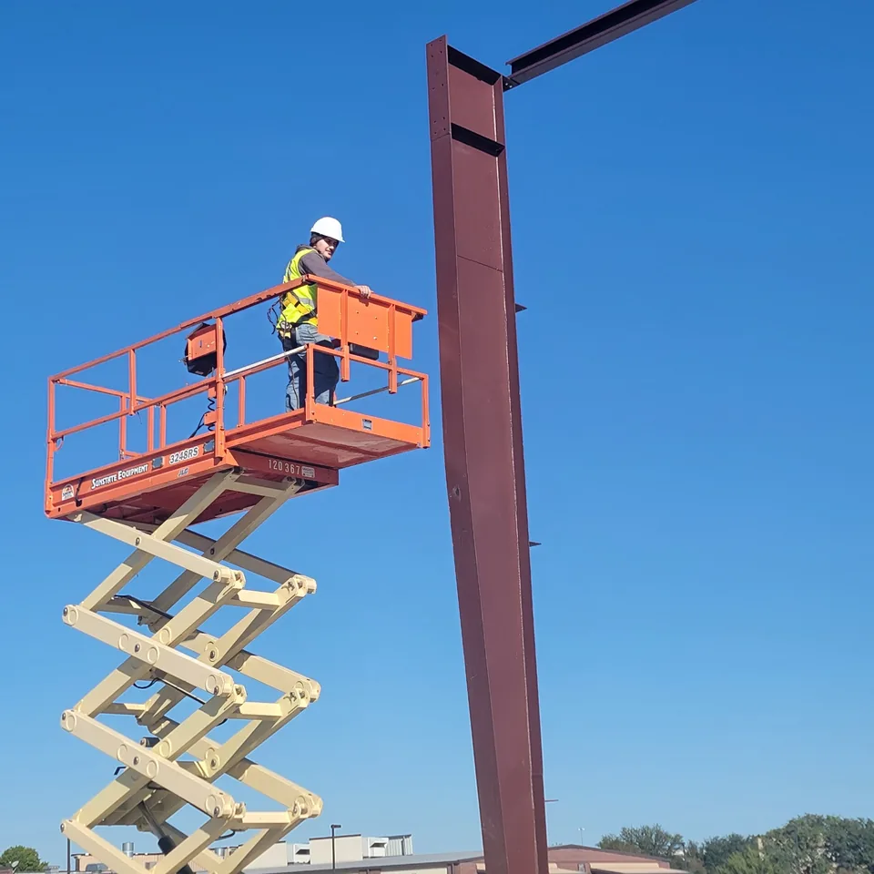 Steel worker on a lift beside commercial structural steel